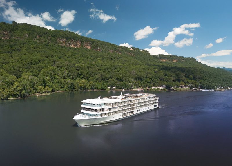 The riverboat American Symphony under way past a wooded bluff