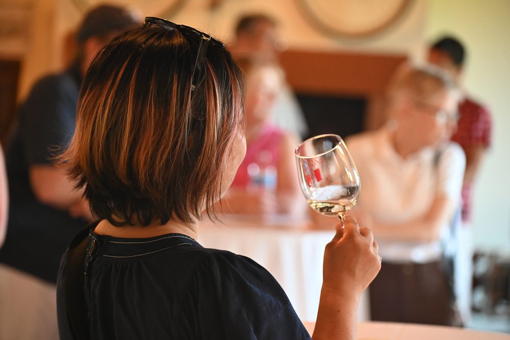 A visitor seen from behind holding a glass of white wine in the Keenan tasting room