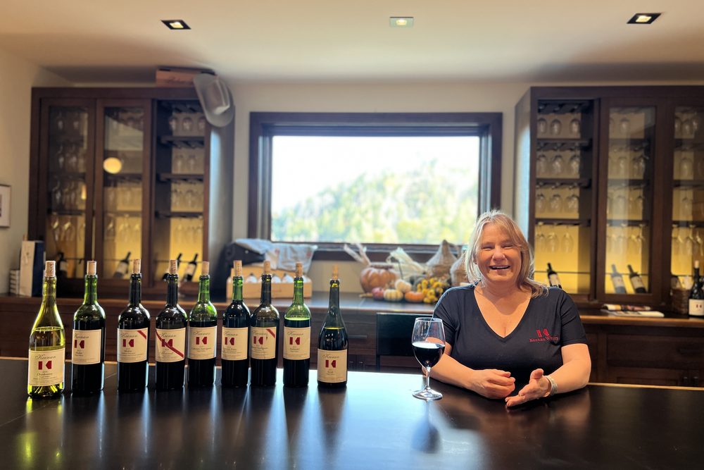 Laura March behind the Keenan tasting bar with a line of bottles and a glass of red wine