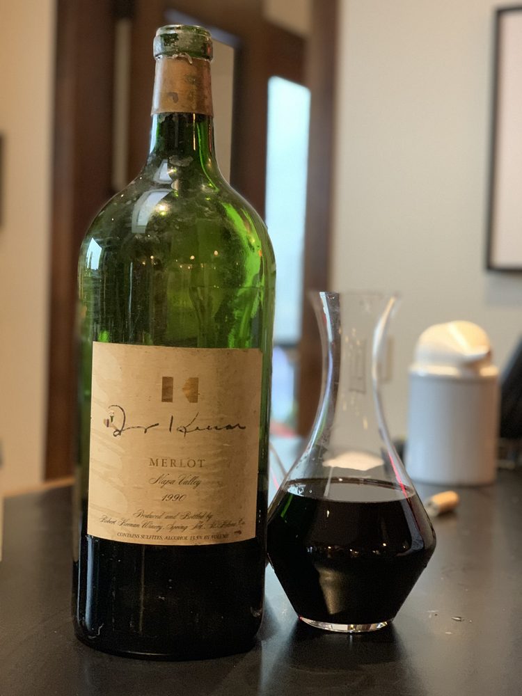 A large-format Keenan Merlot with a hand-signed label standing beside a filled decanter