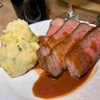 The sliced Wagyu rib eye plated with pan sauce and cheesy garlic smashed potatoes