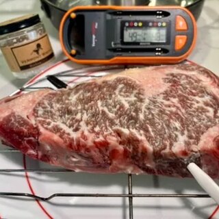 The raw Vermont Wagyu rib eye on a rack with a temperature probe inserted, showing heavy marbling