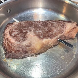 The rib eye searing in a hot stainless steel skillet
