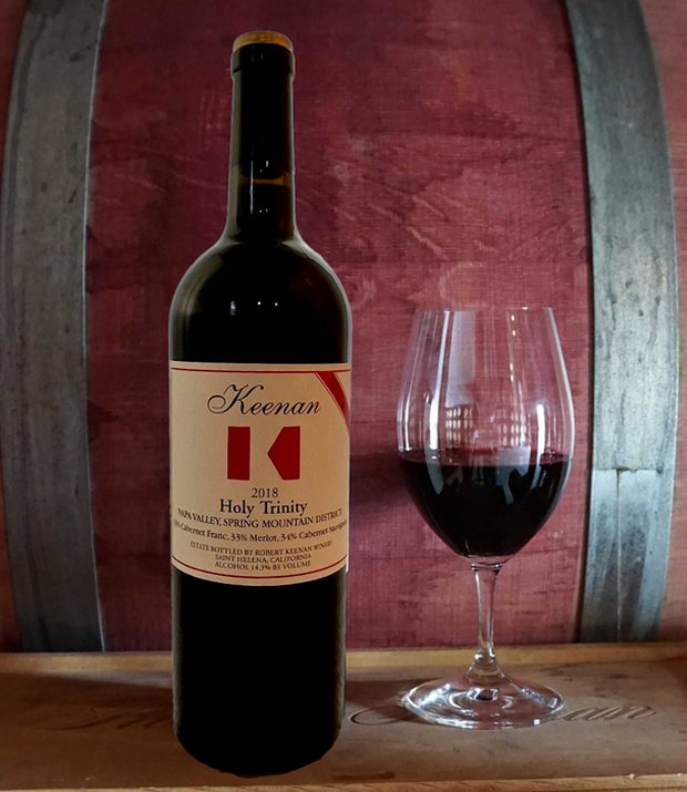 Bottle of Keenan ‘Holy Trinity’ secret reserve red with a poured glass, against the barrel room