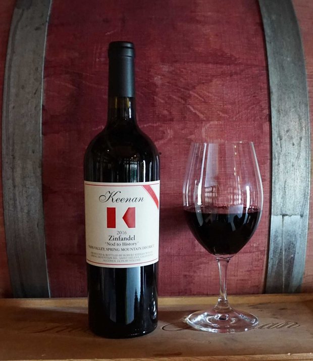 Bottle of Keenan ‘Nod to History’ secret reserve Zinfandel with a poured glass, against the barrel room
