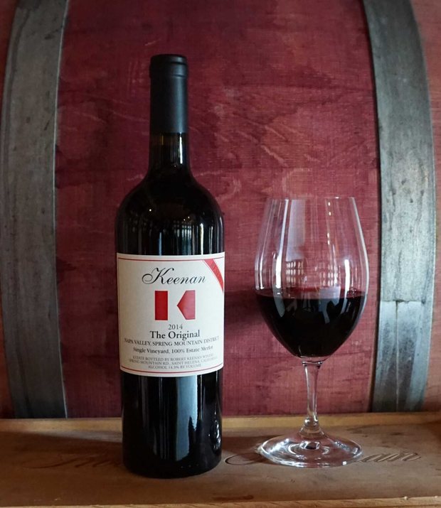 Bottle of Keenan ‘The Original’ secret single-vineyard Merlot with a poured glass, against the barrel room
