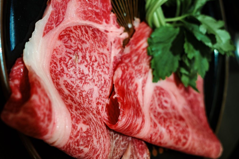 A close crop of heavily marbled wagyu strip steak on a dark plate with fresh parsley