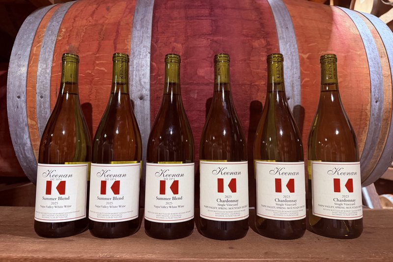 The Keenan White Wine Club shipment against a barrel — three bottles of 2025 Summer Blend and three of the 2023 Single Vineyard Chardonnay
