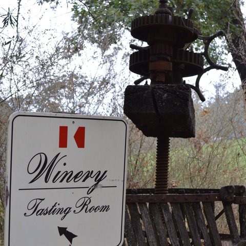 The Keenan Winery tasting room sign with the red K in front of an antique wooden grape press