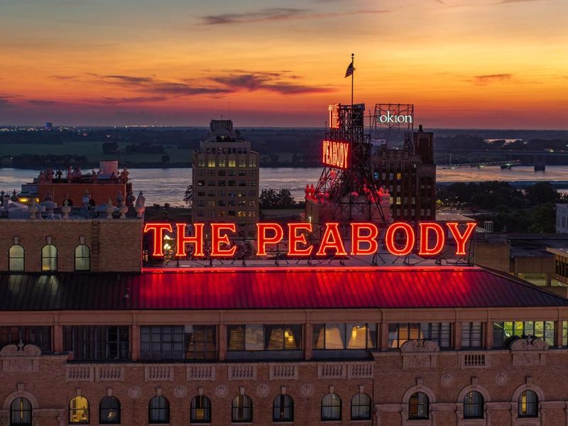 The Peabody hotel's red neon rooftop sign in Memphis at sunset
